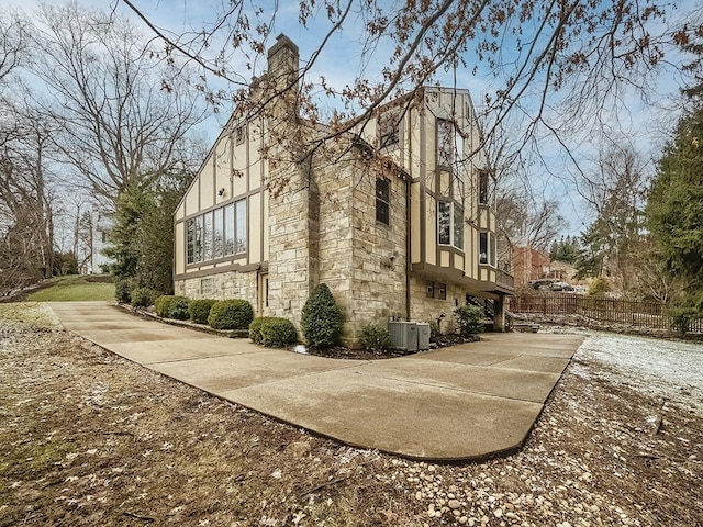 view of side of home featuring stone siding, fence, and stucco siding