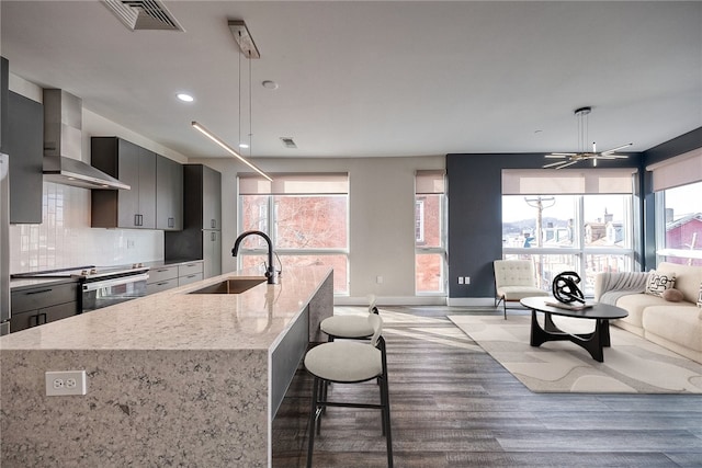 kitchen with visible vents, electric range, open floor plan, a sink, and wall chimney exhaust hood