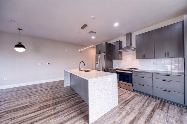 kitchen featuring stainless steel appliances, wood finished floors, a sink, wall chimney range hood, and backsplash