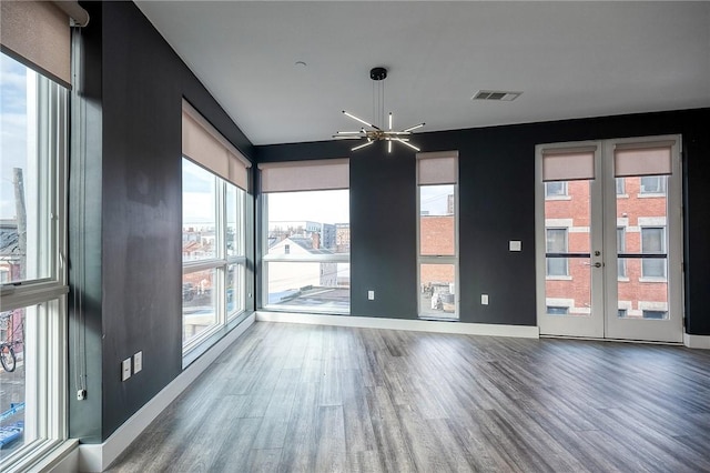 empty room featuring french doors, visible vents, wood finished floors, a chandelier, and baseboards