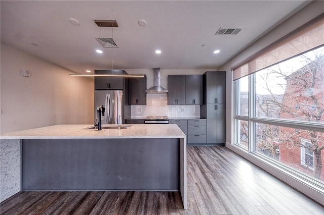 kitchen featuring visible vents, wall chimney range hood, a sink, and appliances with stainless steel finishes