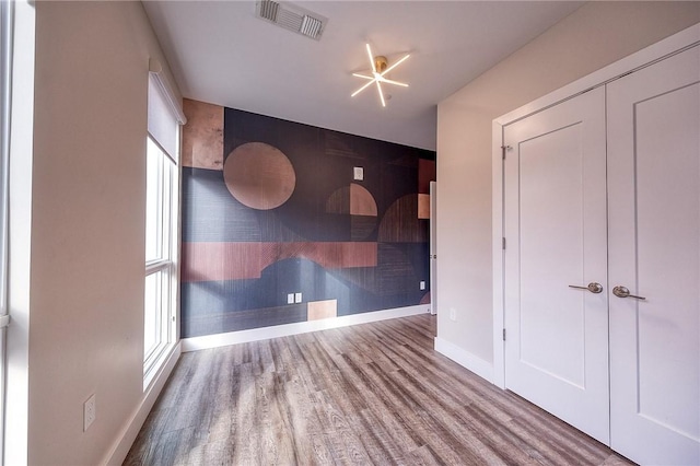 unfurnished room featuring baseboards, an accent wall, visible vents, and wood finished floors