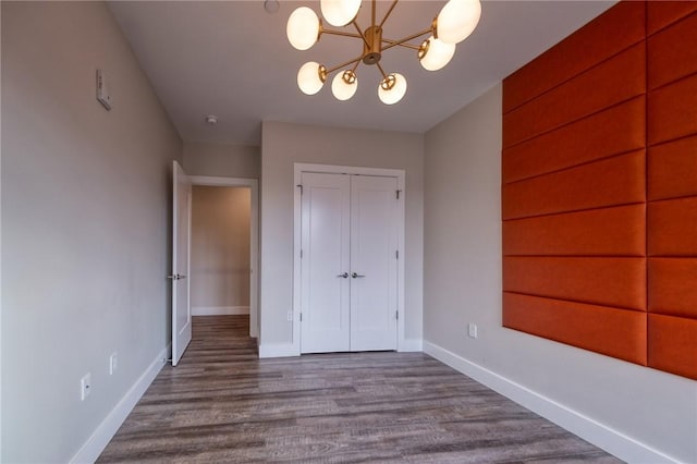 unfurnished bedroom featuring dark wood-style floors, baseboards, a chandelier, and a closet