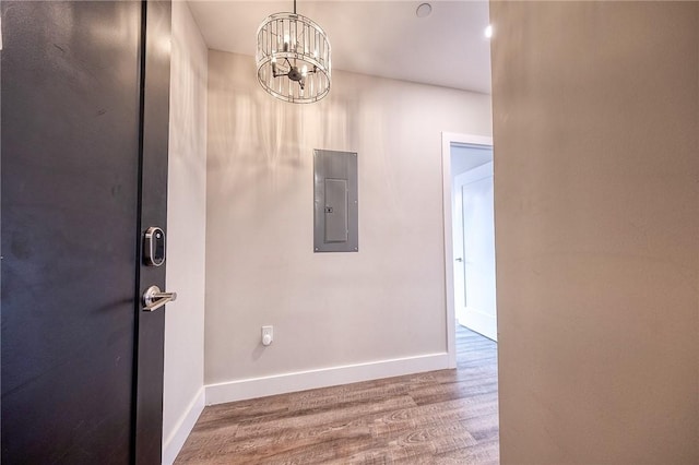 interior space with an inviting chandelier, electric panel, baseboards, and wood finished floors