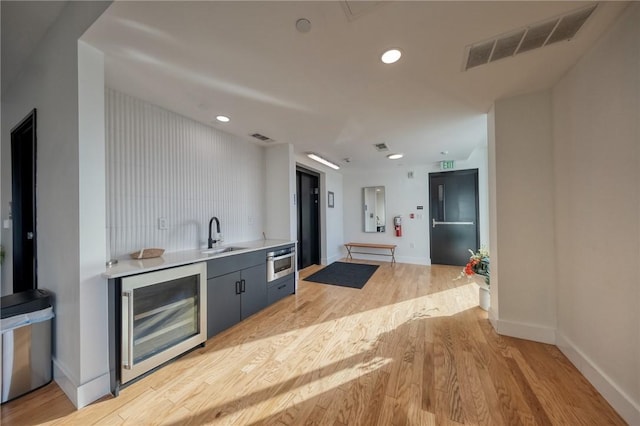 kitchen with wine cooler, a sink, visible vents, light wood-type flooring, and elevator