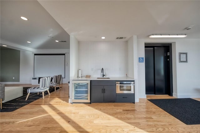 bar featuring light wood-style flooring, oven, beverage cooler, a sink, and elevator