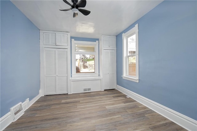 unfurnished bedroom with multiple closets, baseboards, visible vents, and wood finished floors