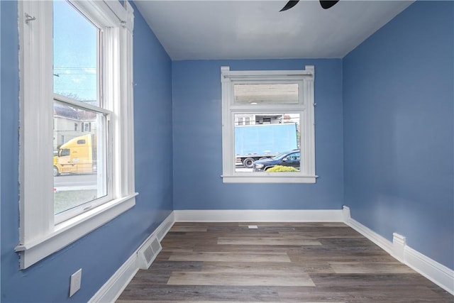 empty room featuring a healthy amount of sunlight, visible vents, baseboards, and wood finished floors