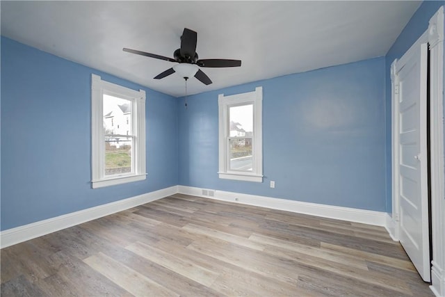 empty room featuring a ceiling fan, wood finished floors, visible vents, and baseboards