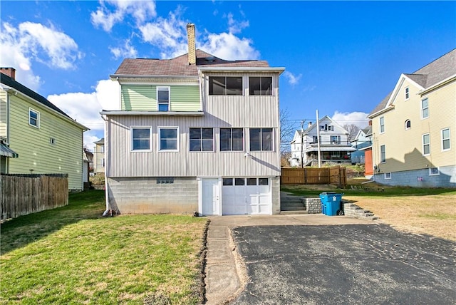 back of house with a garage, fence, a yard, concrete driveway, and a chimney