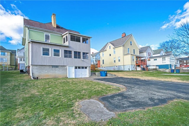 back of property featuring aphalt driveway, an attached garage, a lawn, a residential view, and a chimney