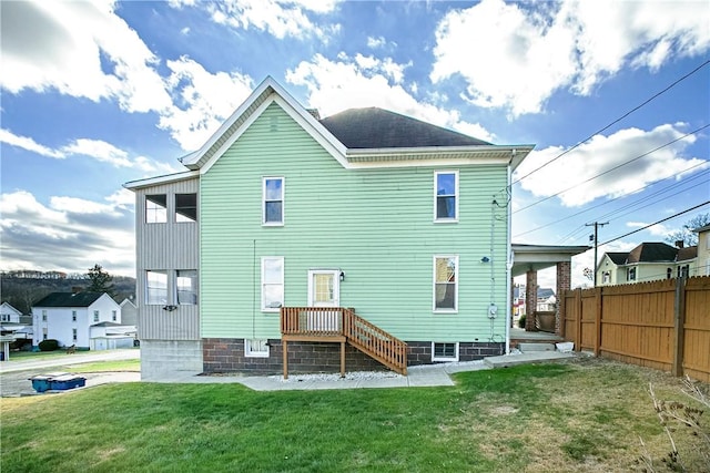 back of house featuring roof with shingles, a lawn, and fence