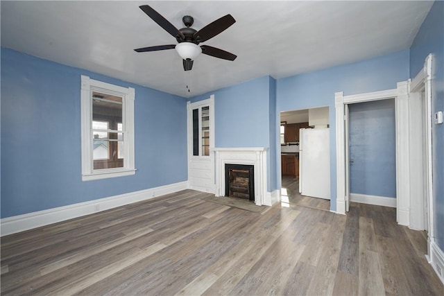 unfurnished living room featuring a fireplace with flush hearth, baseboards, ceiling fan, and wood finished floors
