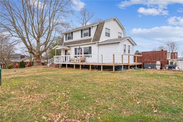 back of house with a yard, roof with shingles, a wooden deck, and a gambrel roof