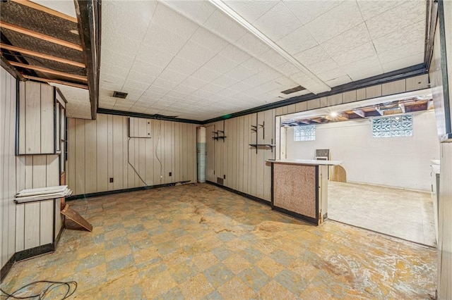 basement with visible vents, wood walls, and tile patterned floors