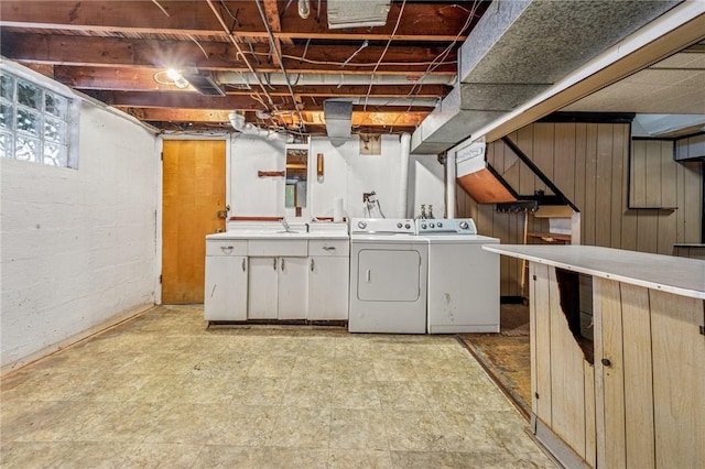 laundry room with wooden walls, separate washer and dryer, a sink, cabinet space, and light floors