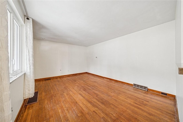 unfurnished room featuring hardwood / wood-style flooring, visible vents, and baseboards