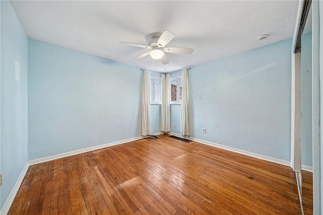 empty room with a ceiling fan, wood-type flooring, visible vents, and baseboards