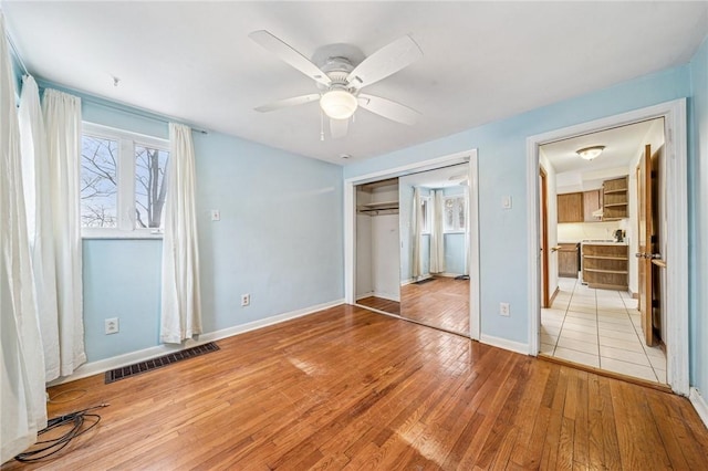 unfurnished bedroom with ceiling fan, light wood-style flooring, visible vents, baseboards, and a closet