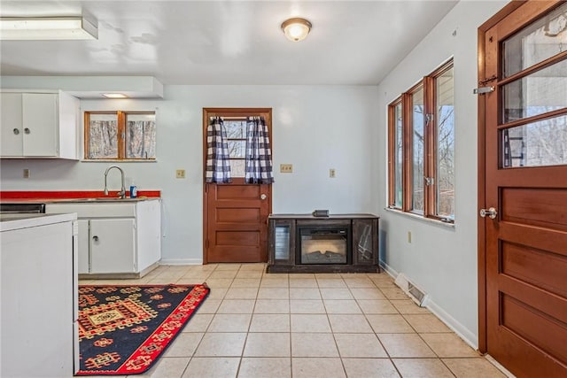 kitchen featuring light tile patterned floors, baseboards, visible vents, white cabinets, and a sink