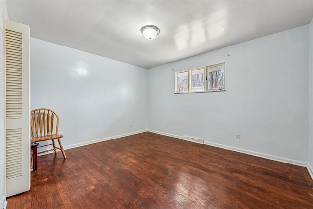 spare room with dark wood-type flooring, visible vents, and baseboards