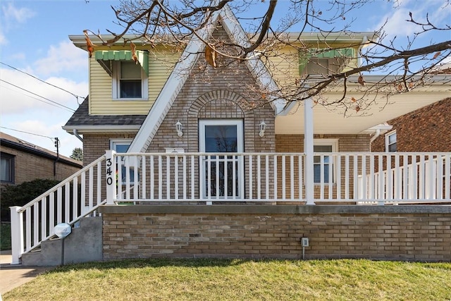 rear view of house featuring a porch, brick siding, and a shingled roof