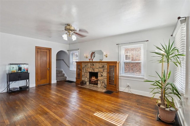 living room with baseboards, arched walkways, hardwood / wood-style floors, stairs, and a stone fireplace