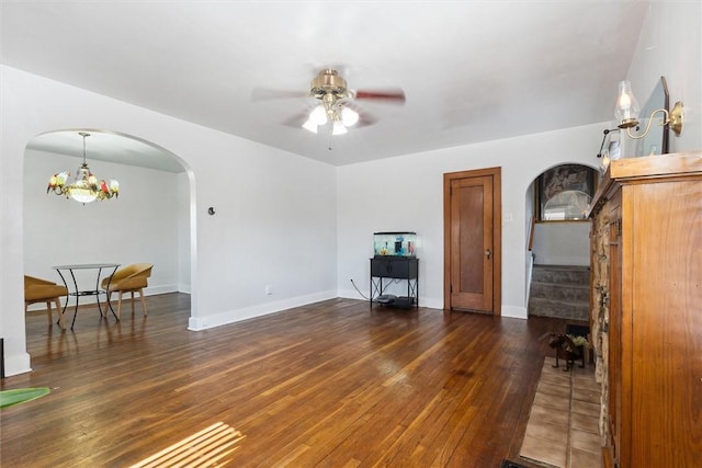 living room featuring dark wood-style floors, arched walkways, stairs, baseboards, and ceiling fan with notable chandelier