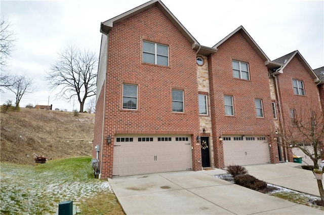 townhome / multi-family property with a garage, concrete driveway, brick siding, and stone siding