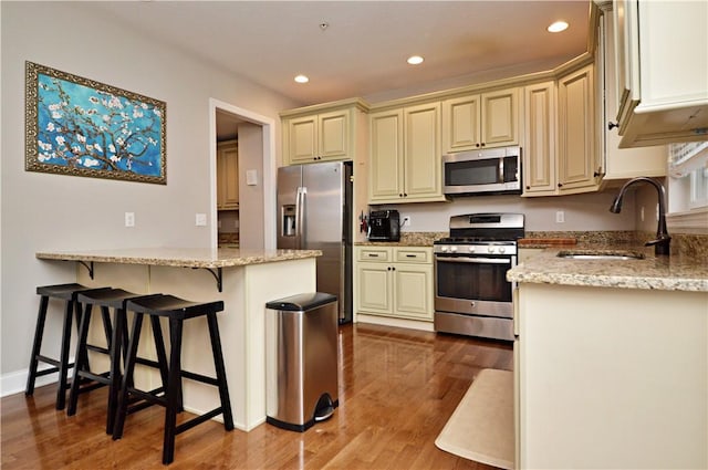 kitchen with stainless steel appliances, light stone counters, cream cabinets, and a sink