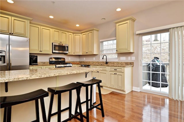 kitchen with cream cabinets, appliances with stainless steel finishes, light wood-style floors, a sink, and a kitchen bar