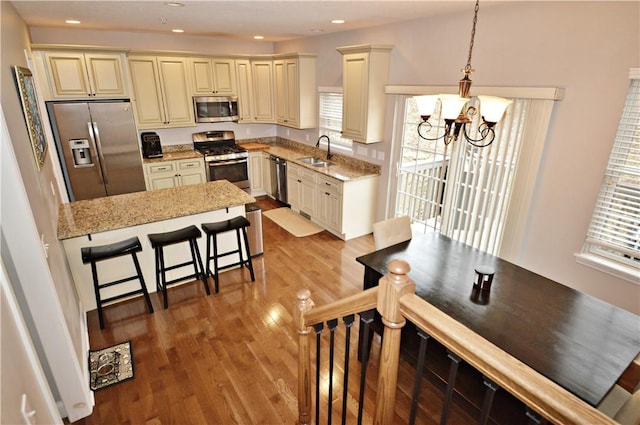 kitchen with light stone counters, stainless steel appliances, light wood-style flooring, cream cabinets, and a sink