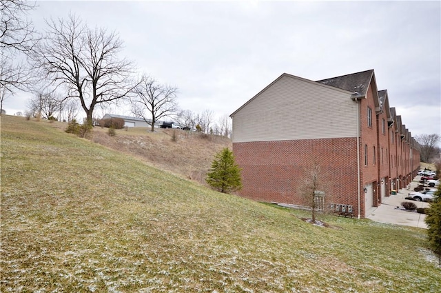 view of home's exterior with concrete driveway, brick siding, a yard, and an attached garage