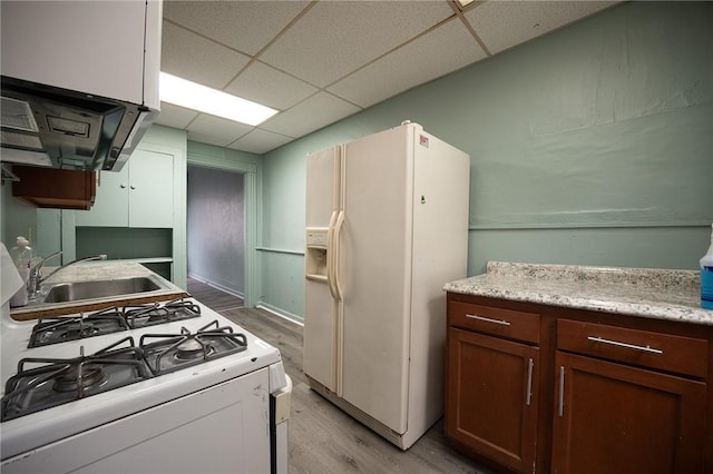 kitchen with light wood-type flooring, white appliances, a drop ceiling, and a sink