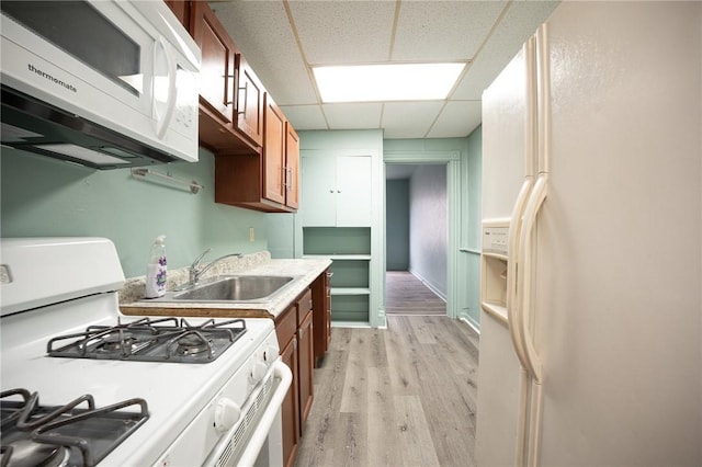 kitchen featuring brown cabinets, a paneled ceiling, light wood-style floors, a sink, and white appliances