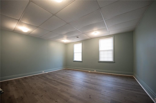 empty room with a drop ceiling, dark wood finished floors, and baseboards