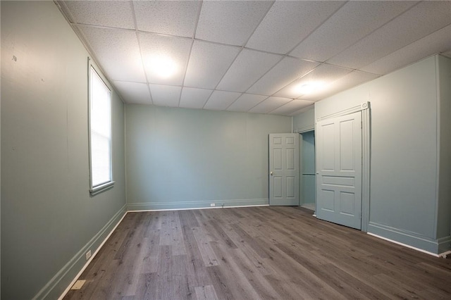 spare room with a drop ceiling, wood finished floors, and baseboards