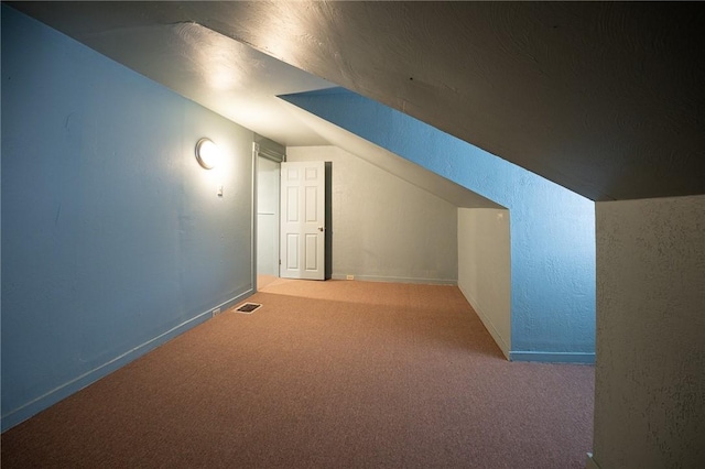 additional living space featuring carpet, visible vents, a textured wall, and lofted ceiling