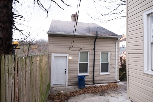 rear view of property with a shingled roof, a chimney, and fence