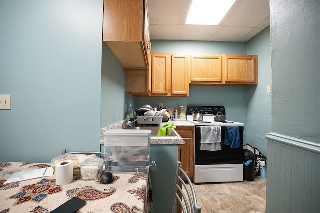 kitchen with a drop ceiling, a sink, electric stove, light countertops, and light brown cabinetry