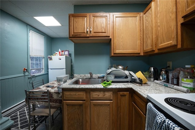 kitchen with white appliances, a drop ceiling, wainscoting, a baseboard radiator, and a sink