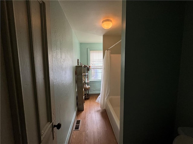 bathroom featuring a textured wall, shower / tub combo, wood finished floors, and visible vents