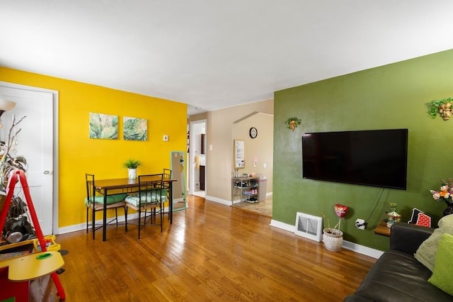 living room with an accent wall, wood finished floors, visible vents, and baseboards