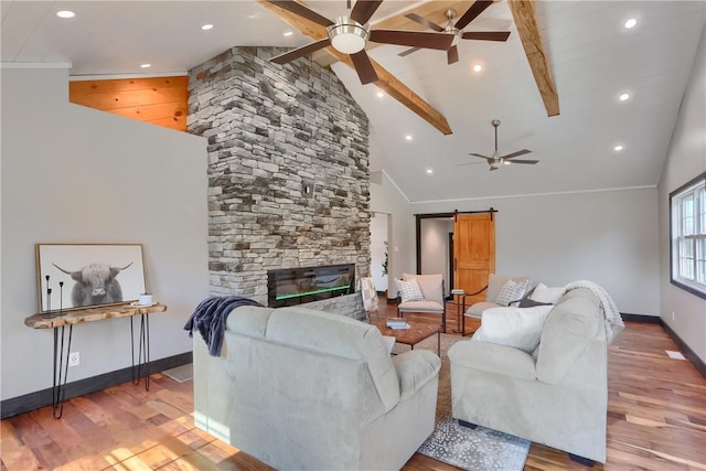 living room with a stone fireplace, a barn door, wood finished floors, and baseboards