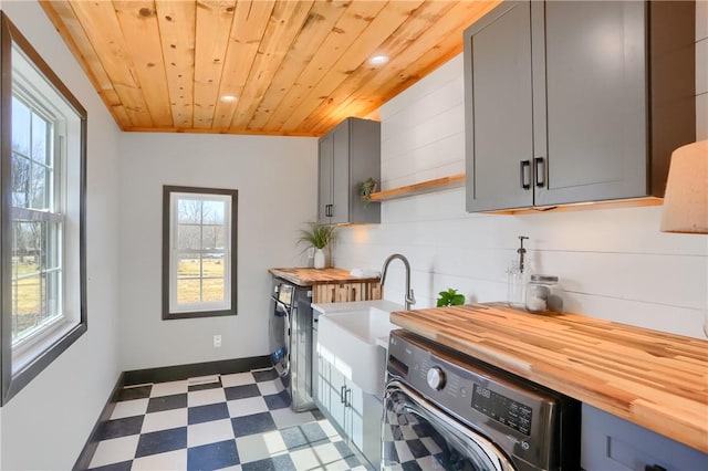 laundry area featuring dark floors, cabinet space, washer / dryer, wooden ceiling, and baseboards