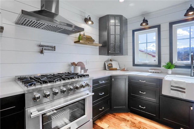 kitchen featuring stainless steel stove, a sink, light countertops, light wood-type flooring, and wall chimney exhaust hood