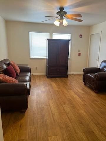 living area featuring ceiling fan, light wood-style flooring, and baseboards