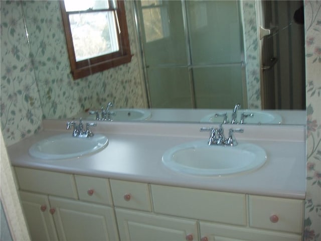 full bathroom featuring double vanity, a sink, and wallpapered walls