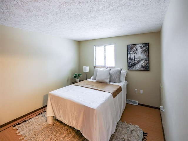 bedroom featuring baseboards, a textured ceiling, visible vents, and wood finished floors