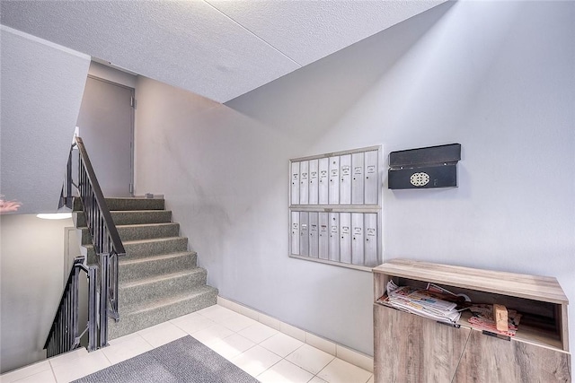 stairway with a textured ceiling, vaulted ceiling, tile patterned flooring, and mail area